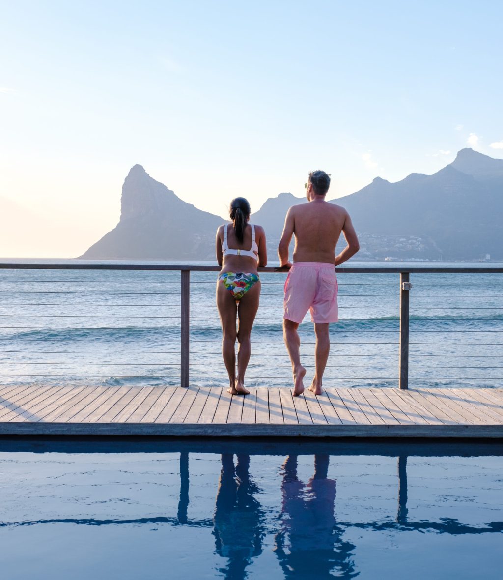 a mature couple man and woman in front of Infinity pool looking out over the ocean of Cape Town South Africa, man and woman in a swimming pool during sunset.