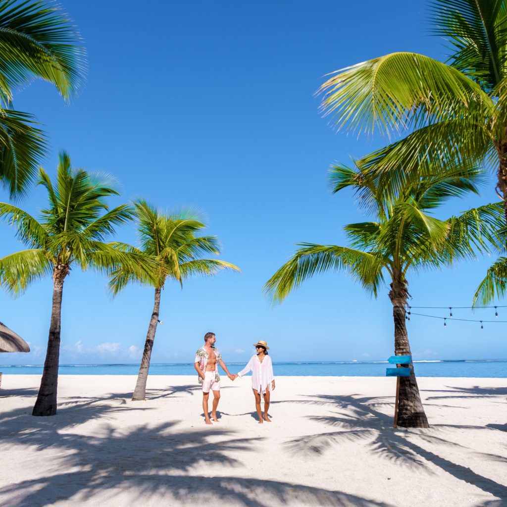 Man and Woman on a tropical beach with beach chairs and palm trees in Mauritius, a couple on a honeymoon vacation in Mauritius Le Morne Beach with Le Morne Mountain on the background