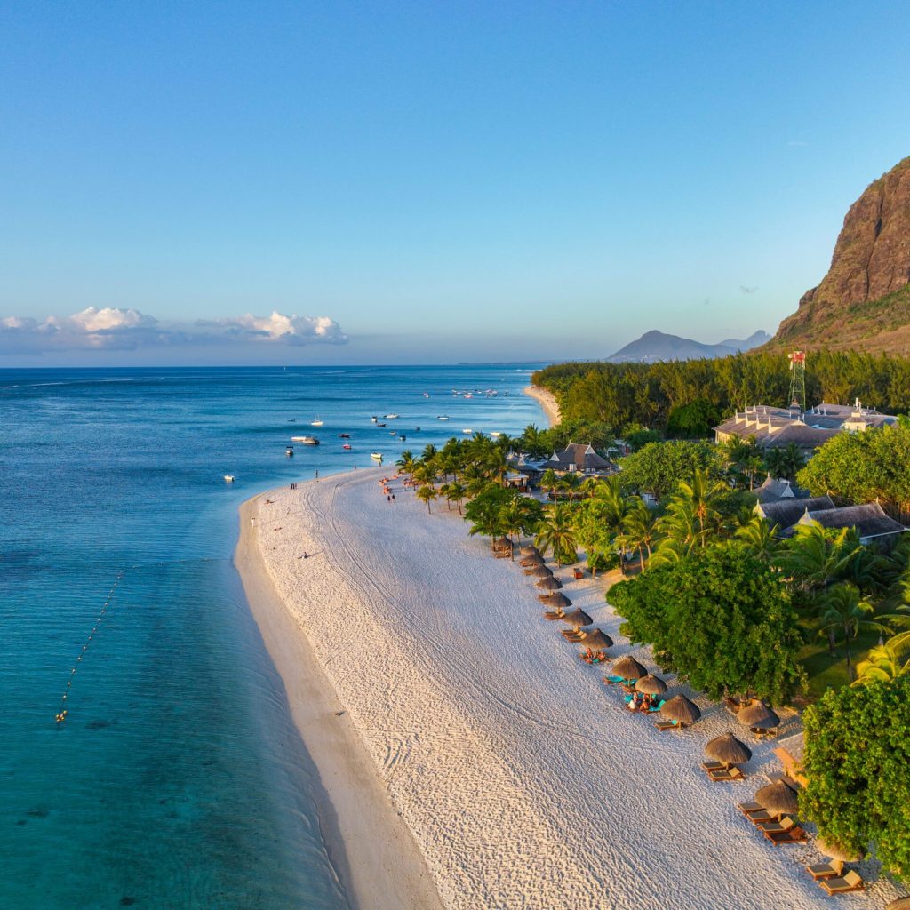 Morning sunlight illuminates the curve of the beach and calm sea surrounding the peninsula of Le Morne, Mauritius